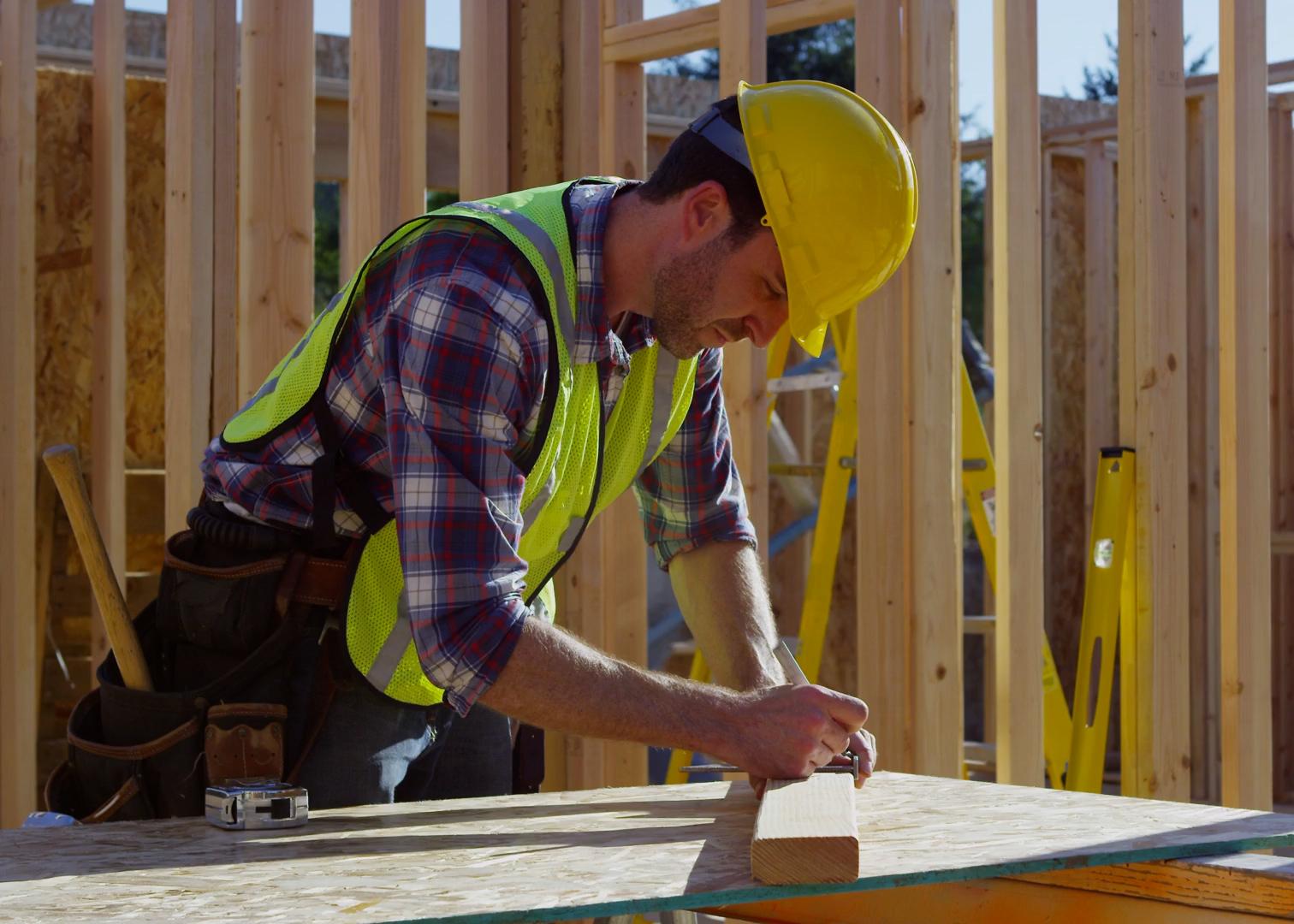 a man in a hard hat measuring a piece of timber